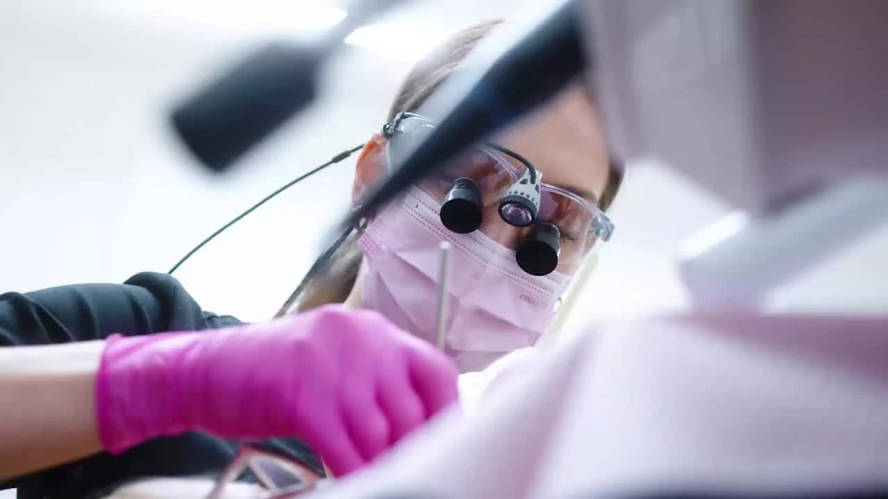 Zubní lékařka s lupovými brýlemi při ošetření pacienta
